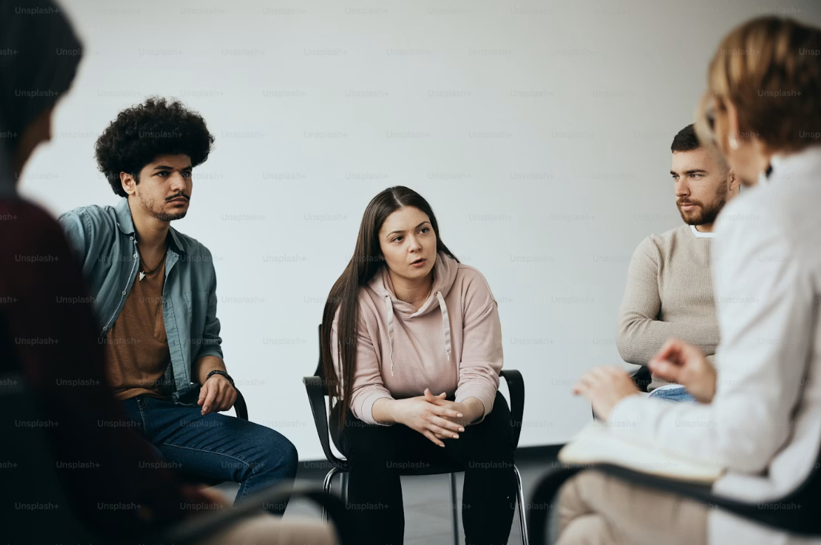 A diverse group of adults sitting together in a supportive circle in a warm, naturally lit room